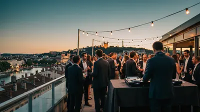 Company drinks on a Lyon rooftop at dusk, a DJ in a suit seen from behind, Fourvière on the skyline