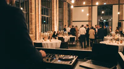Seminar evening in a brick hall, seen from the DJ booth, guests standing between the tables