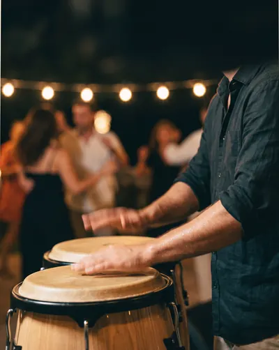 Mains sur des congas, invités qui dansent sous les guirlandes