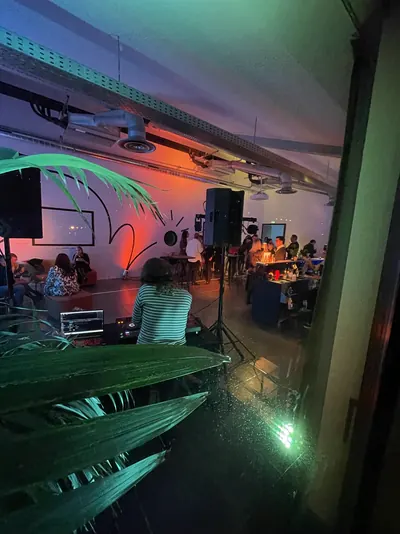 DJ seen from behind in a loft, orange light, guests around the bar
